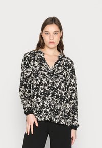 Blusa preta com padrão floral branco, decote em V, mangas longas e detalhes em botão. O tecido é suave com uma textura leve.