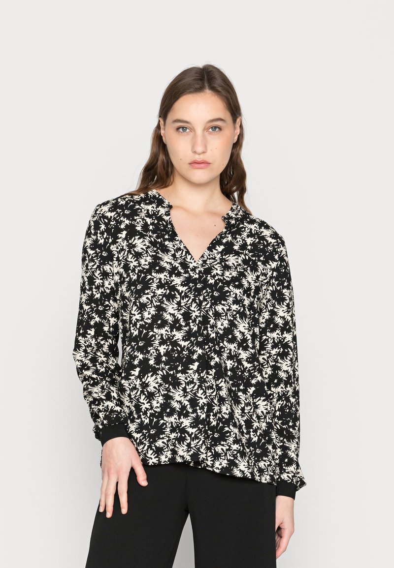 Blusa preta com padrão floral branco, decote em V, mangas longas e detalhes em botão. O tecido é suave com uma textura leve.