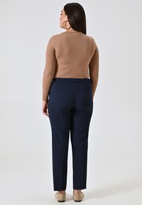 Maglione di maglia beige e pantaloni stretchy blu scuro con cintura elastica. Tessuto liscio, vestibilità aderente e un'unica tasca sul retro dei pantaloni.