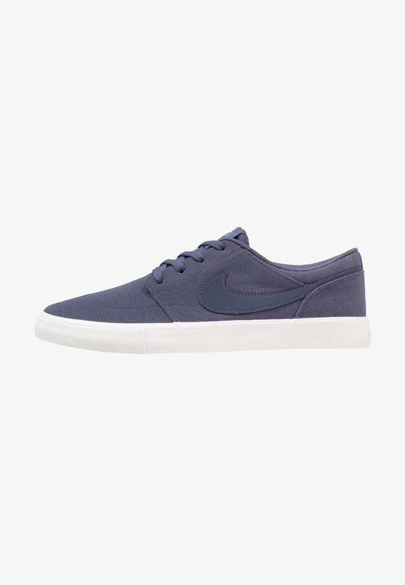 Baskets basses bleu foncé avec dessus en tissu, fermeture à lacets, logo Nike sur le côté, et semelle en caoutchouc blanche.