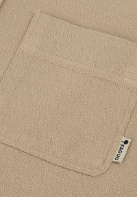 Tessuto beige con texture, dotato di una tasca frontale, caratterizzato da un orlo cucito e un piccolo etichetta con un logo. La superficie presenta un aspetto intrecciato.