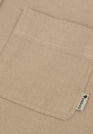 Tessuto beige con texture, dotato di una tasca frontale, caratterizzato da un orlo cucito e un piccolo etichetta con un logo. La superficie presenta un aspetto intrecciato.