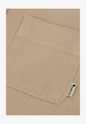 Beige texturiertes Gewebe mit einer Vordertasche, die eine genähte Kante und ein kleines Etikett mit einem Logo aufweist. Die Oberfläche hat ein gewebtes Aussehen.