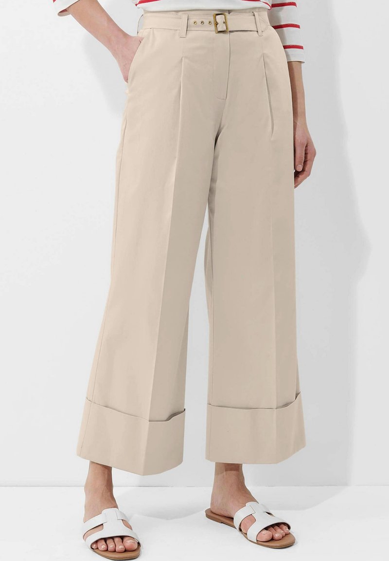 Beige weite Hose mit hohem Bund, Falten und einem taillierten Design. Verfügt über eine saubere, glatte Textur und einen umgeschlagenen Saum.