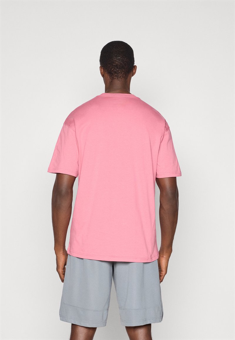 T-shirt a maniche corte in cotone rosa chiaro, con collo tondo e vestibilità rilassata, abbinato a pantaloni corti sportivi grigi.
