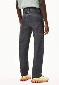 Donkergrijze corduroy broek met een relaxte pasvorm, voorzien van een achterzak met branding en gecombineerd met gele en blauwe sneakers.