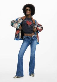 Värvikas lapitehnikaga jakk, must graafiline T-särk, sinised laiade säärega teksad ja beežid tossud; tekstuuriga kangas, lõdva lõikega, vabaaja disain.