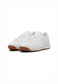 White sneaker made of leather with a rounded shape, textured rubber outsole in brown, and flat laces; side logo detail embossed.