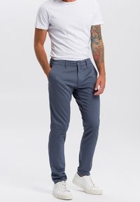 Leichte, figurbetonte graue Chinos mit glatter Textur, Knopfverschluss und Seitentaschen, kombiniert mit einem weißen T-Shirt und weißen Sneakern.