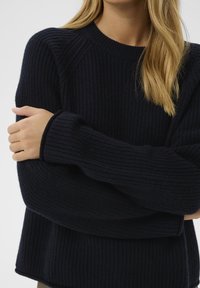 Granatowy sweter o prążkowanej strukturze z okrągłym dekoltem i szerokimi rękawami, charakteryzujący się luźnym krojem i miękką fakturą. Bez widocznych wzorów ani logo.