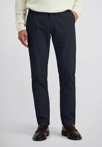 Navyblauwe broek van gladde stof, ontworpen met een klassieke pasvorm. Heeft voorzakken en een middelhoge tailleband; gecombineerd met bruine schoenen.