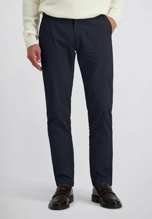 Navyblauwe broek van gladde stof, ontworpen met een klassieke pasvorm. Heeft voorzakken en een middelhoge tailleband; gecombineerd met bruine schoenen.