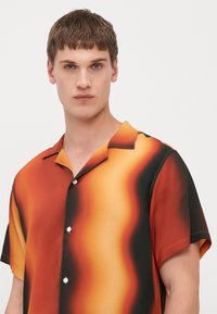 Camisa de manga corta con un patrón de degradado en tonos naranjas y negros, fabricada en tejido suave y con cierre de botones y cuello.