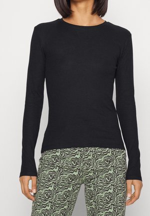 Haut noir à manches longues en maille côtelée avec un col rond et une coupe ajustée, associé à un pantalon vert et noir à motifs ondulés.