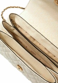 Sac à main matelassé beige avec une fermeture ton or, une bandoulière chaîne et trois compartiments avec la marque "GUESS" à l'intérieur.