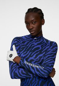 Rashguard z długim rękawem w kolorze niebieskim z czarnymi paskami zebry. Posiada wysoki kołnierz oraz białe logo na rękawie. Teksturowany, elastyczny materiał.