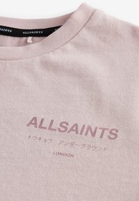 Hellrosa AllSaints T-Shirt mit geripptem Kragen und gedrucktem AllSaints London Logo sowie japanischen Schriftzeichen auf der Brust.
