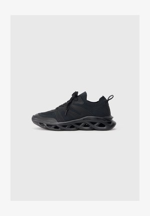 Zapatillas deportivas negras con parte superior de malla y suela curva, con corte redondeado y acentos texturizados. Incluye cordones y una lengüeta.