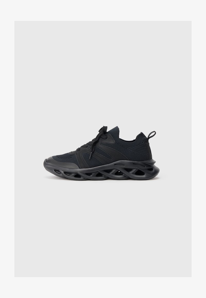 Zwarte sportieve schoenen met een bovenwerk van mesh en een gebogen zool, voorzien van ronde uitsparingen en getextureerde accenten. Inclusief veters en een trekstrip.