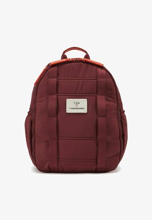 Bordeaux gekleed rugzak met gewatteerde textuur, oranje ritsdetails en een zilveren logo plaat. Beschikt over dubbele draagriemen.