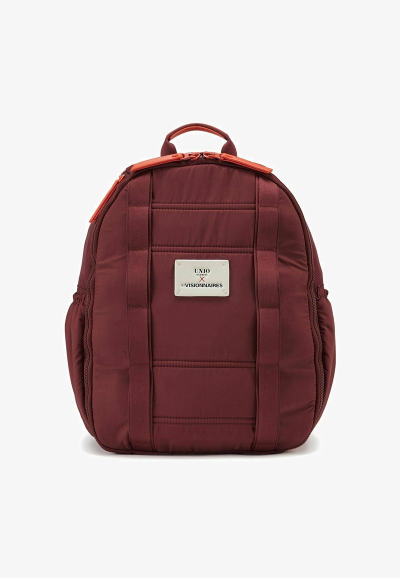 Mochila acolchada color burdeos con textura suave, detalles en cremallera naranja y una placa de logo plateada de marca. Cuenta con correas dobles para llevar.