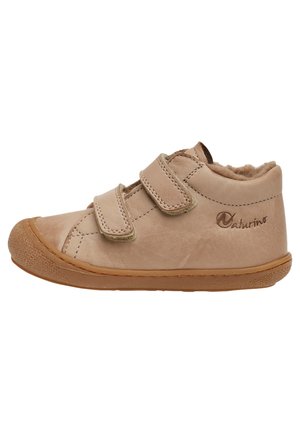 Beige Lederkinderschuh mit doppelten Klettverschlussriemen, runder Zehenform, strukturiertem Gummisole und weichem Fellfutter. Markenlogo sichtbar.