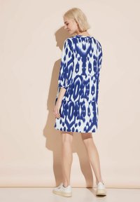 Blau-weiß gemustertes Kleid mit Dreiviertelärmeln, gestuftem Design und Knopfverschluss hinten. Getragen mit weißen Sneakers.