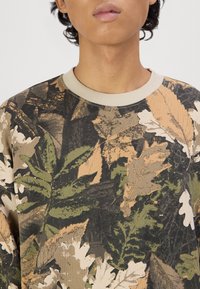 Felpa in cotone con stampa foglia camouflage in tonalità di verde, beige e marrone, con colletto a girocollo in beige a costine.