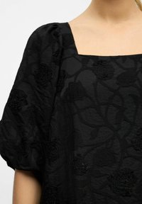 Vestido negro con escote cuadrado y mangas abullonadas, adornado con bordados florales texturizados y un patrón tejido.