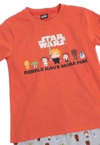 Camiseta de algodón naranja con el logo de "Star Wars" y personajes pixelados con el texto "LOS REBELDES SE DIVIERTEN MÁS." Pantalones de pijama grises con patrones de personajes.