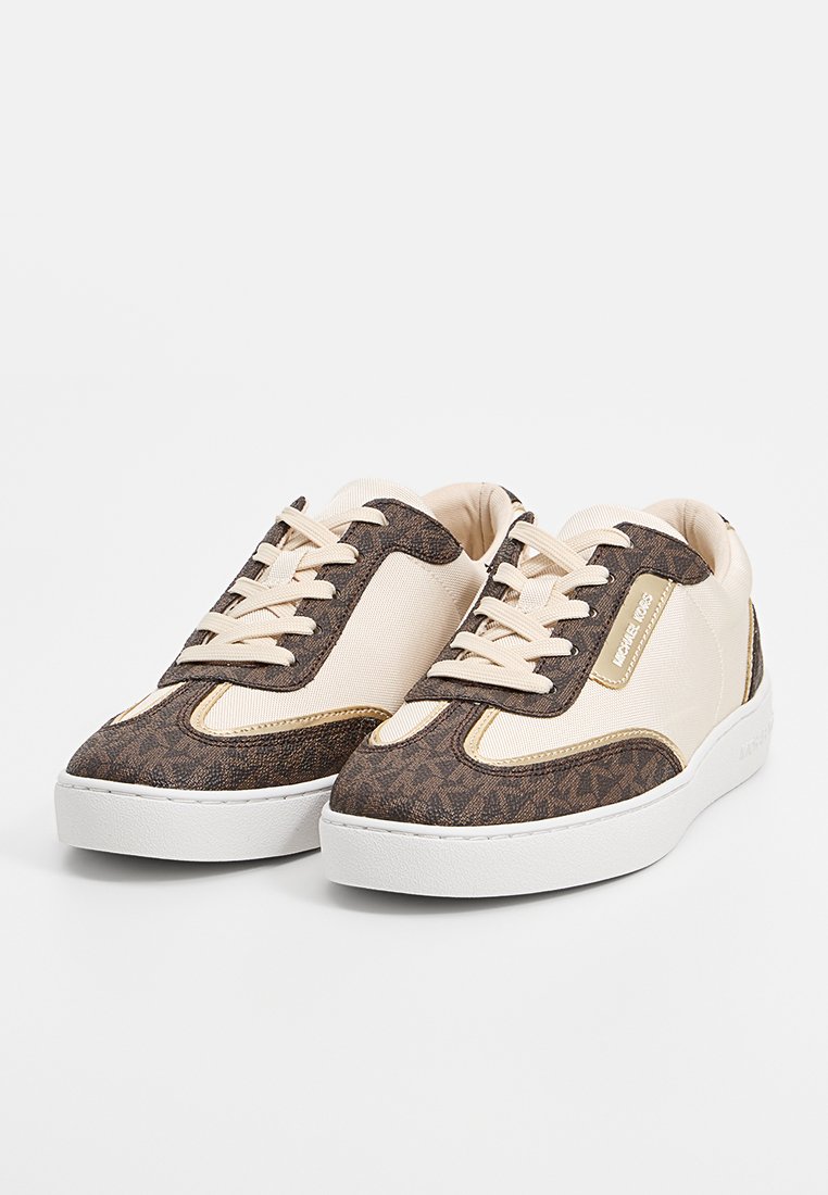 Baskets marron et crème avec une tige texturée, semelle en caoutchouc blanc et lacets contrastants. Présente un détail de logo sur le côté et des accents contrastants.