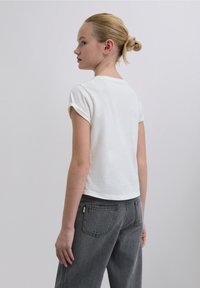 T-shirt bianca in cotone a maniche corte con scollo rotondo, indossata con jeans grigio scuro a vita alta. Design minimalista e taglio corto.