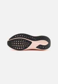 Semelle de chaussure de sport noire et rose avec une surface texturée présentant des motifs circulaires et hexagonaux pour une traction optimale. Matériau lisse et flexible.