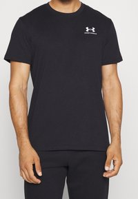 T-shirt in cotone nero con collo a giro, maniche corte e logo bianco Under Armour nella parte superiore sinistra del petto.