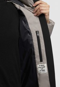 Black and gray jacket with a shiny fabric interior, zippered pocket, and a tag stating "A warm hug made out of cloth."