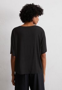 Czarna, oversize koszulka z miękkiego, gładkiego materiału, z szerokim dekoltem i krótkimi rękawami, charakteryzująca się prostym, czystym wzorem bez zdobień.