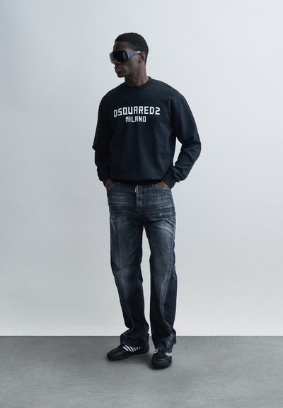 Schwarzer Sweatshirt mit "DSQUARED2 MILANO" in Weiß, kombiniert mit dunklen Denim-Jeans mit Reißverschlüssen. Schwarze Sneaker mit weißen Streifen.