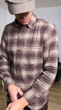 Brown plaid flannel shirt with gray, cream, and maroon checks, featuring a buttoned front and a chest pocket. Smooth texture, long sleeves.