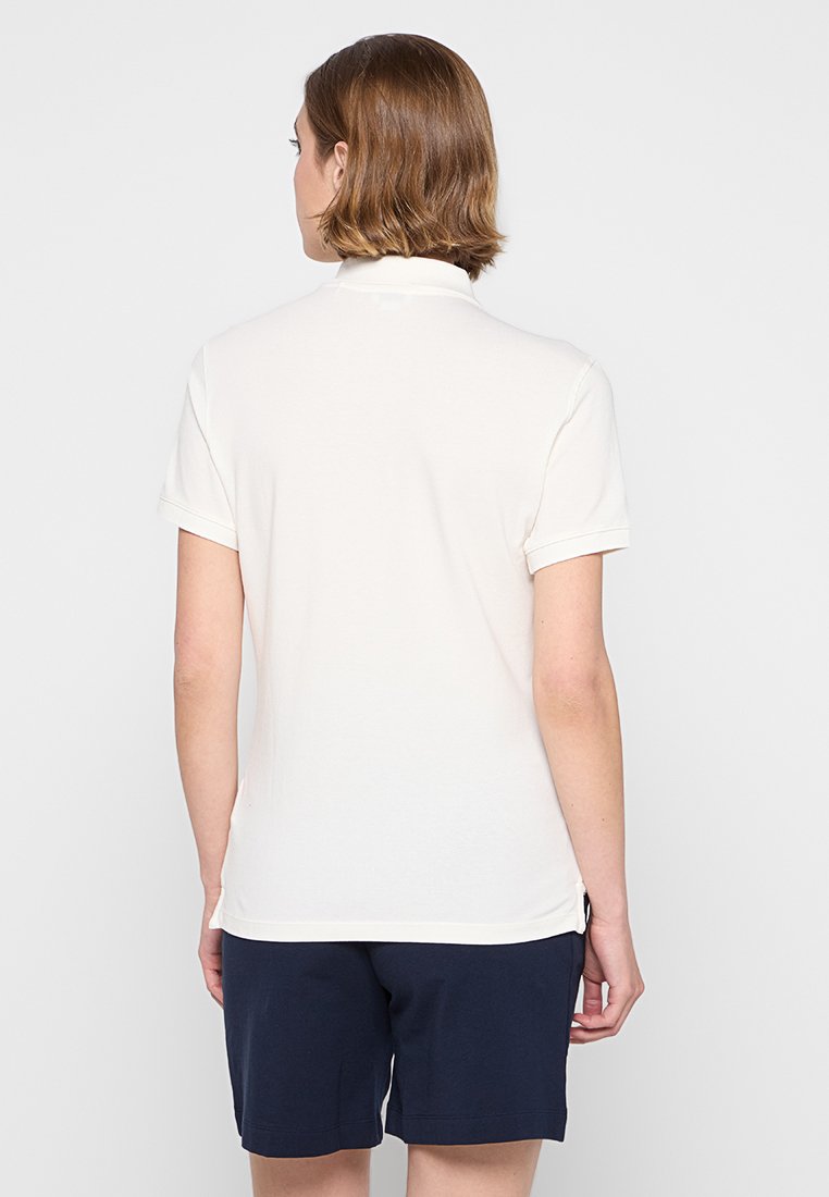 Polo shirt bianco a maniche corte con una texture morbida e colletto. Presenta maniche arrotolate e orlo dritto. Indossato con pantaloni corti blu navy.