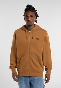 Brown zip-up hoodie made from soft fabric, featuring a kangaroo pocket, drawstring hood, and a small logo on the chest.