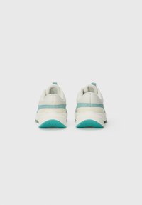 Sneaker mit einem weißen Obermaterial und hellblauen Akzenten sowie einer strukturierten Türkissohle. Abgerundete Form mit auffälligen Dämpfungsdetails.