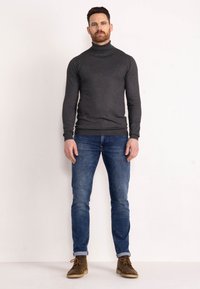Pulover gri cu guler înalt, design ajustat, asortat cu blugi slim-fit de culoare albastru închis și cizme scurte maro. Material neted, accente minime.