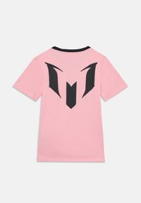 Rosa t-skjorte med kort erm og et svart grafisk design på baksiden som ligner et stilisert emblem. Har svart krave. Myk tekstur.