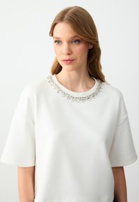 Witte sweatshirt met korte mouwen, voorzien van een decoratieve kraal decolleté. Soepele textuur en ontspannen pasvorm. Eenvoudig en modern ontwerp.