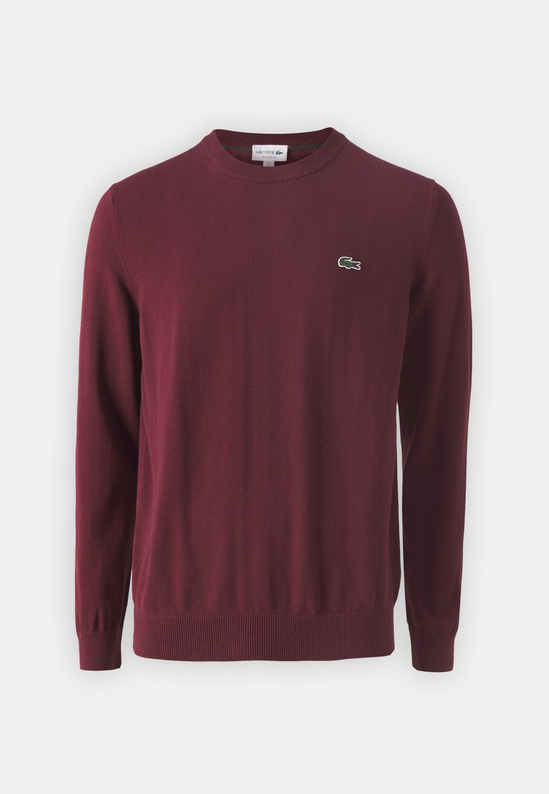 Pull en bordeaux à col rond en tissu tricoté doux, avec des manches longues et un petit logo vert sur la poitrine gauche.