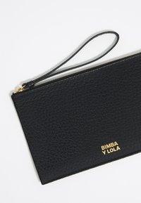 Zwarte leren pouch met een getextureerde oppervlakte, gouden rits en een polsband. Gouden "BIMBA Y LOLA" logo op de voorkant. Minimalistisch ontwerp.