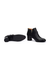 Botas negras hasta el tobillo hechas de cuero suave, con punta redonda, cremallera lateral y tacón apilado. Suela de goma texturizada para mayor agarre.