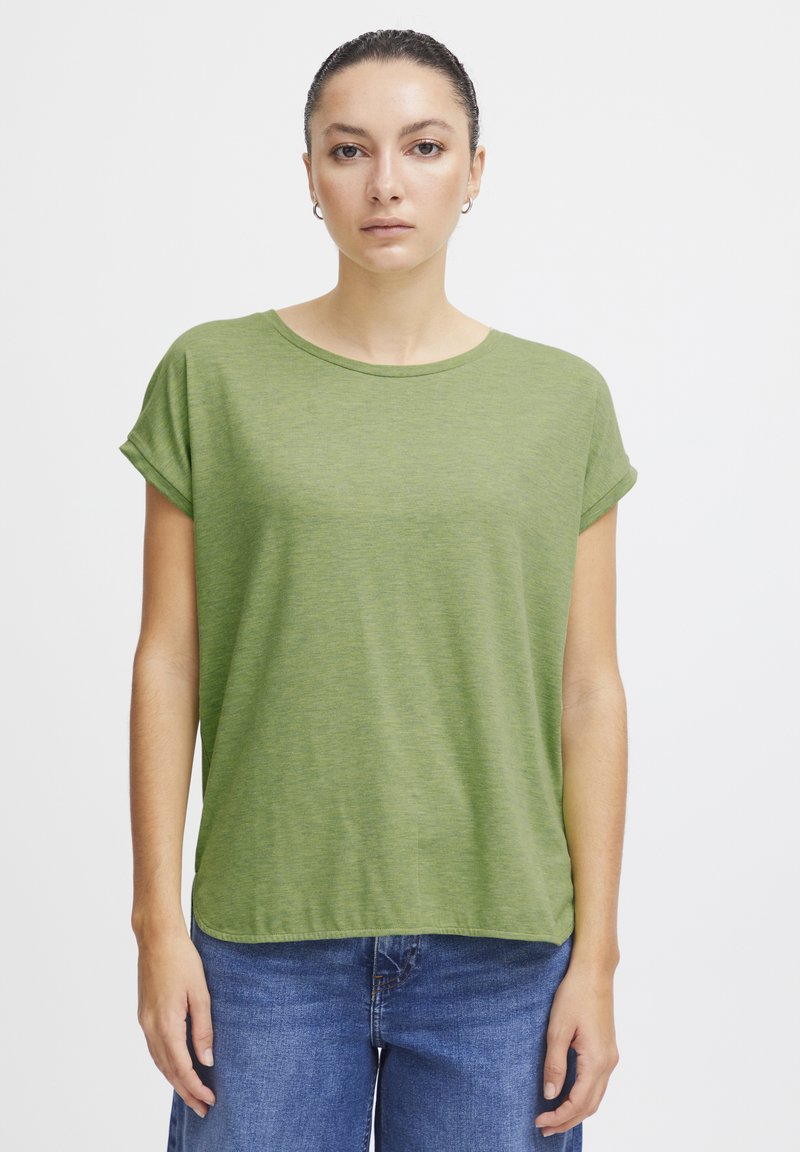 Camiseta verde de manga corta hecha de tela suave con cuello redondo y un ajuste holgado, combinada con pantalones vaqueros azules. Diseño simple, sin patrones.