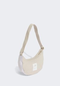 Bolso de hombro beige con forma curva, hecho de tela suave. Cuenta con un panel blanco con un logo y un cierre con cremallera para mayor seguridad.