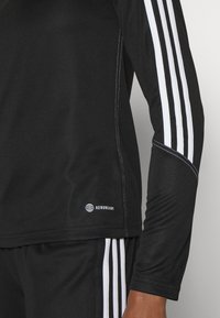 Čierne športové tričko s dlhým rukávom a bielymi prúžkami pozdĺž ramien, s logom "AEROREADY" na spodnom leme. Hladká textúra, priliehavý strih.